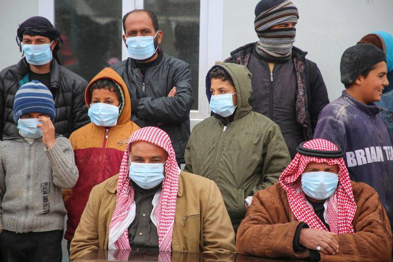 Displaced Syrian, some wearing protective masks, listen as medics hold an awareness campaign on how to be protected against the novel coronavirus pandemic, in a camp for displaced people in Kafr Lusin, in the northwestern province of Idlib, following heavy storms on March 18, 2020. (Photo by Mohammed AL-RIFAI / AFP)