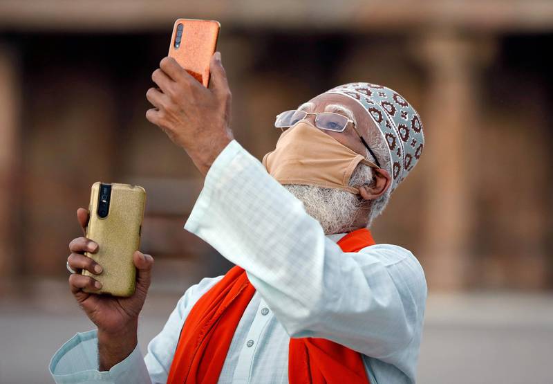 A man wearing a protective mask uses his mobile phone camera as he tries to spot the new moon that marks the start of Ramadan, at a mosque in Ahmedabad, India, April 24, 2020. Reuters