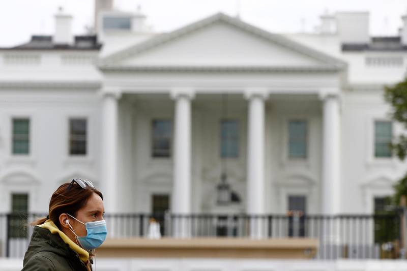 FILE - In this April 1, 2020, file photo a woman wearing a face mask walks past the White House in Washington. Americans are increasingly taking preventative measures, including staying away from large crowds and avoiding touching their hands to their faces, amid growing fears of infection with COVID-19, a new poll from The Associated Press-NORC Center for Public Affairs Research found.  (AP Photo/Patrick Semansky, File)