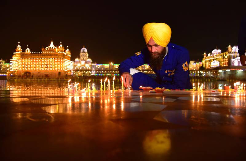 A Sikh man lights candles at an illuminated Golden temple on the eve of the birth anniversary of Guru Nanak in Amritsar, India. AP Photo