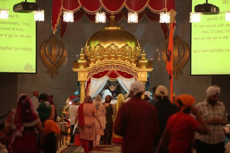 Devotees walk down a diagonal walkway to bow to the Guru Granth Sahib religious text, before sitting on a large soft carpet.