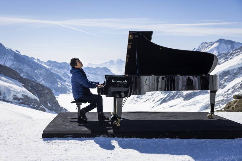 Chinese pianist Lang Lang plays a showcase surrounded by the peaks of Eiger, Moench and Jungfrau and the Aletsch glacier on the Jungfraujoch, Switzerland, Thursday, April 14, 2022.  Lang Lang visited the Top of Europe and uncovered an ice statue in the ice cave.  (Peter Klaunzer / Keystone via AP)