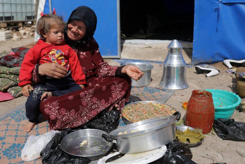 An internally displaced woman with a child on her lap prepares food outside a tent in Azaz, Syria. REUTERS