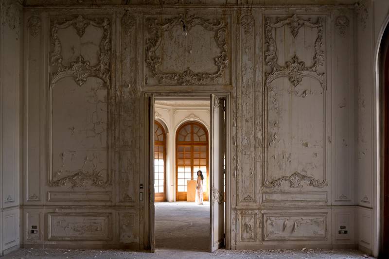 A woman stands in an old mansion in Mazraa, with a crumbling interior decorated in classical French style. Courtesy Gregory Buchakjian