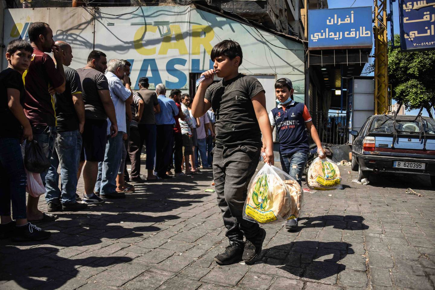 Boys carry packs of bread past people queuing at a bakery in Tripoli as shortages continue to worsen. Elizabeth Fitt for The National