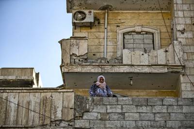 A woman stands in front of a bullet riddled facade in the northern Syrian city of Raqa, the former Syrian capital of the Islamic State (IS) group, on August 21, 2019. - The Kurdish-led Syrian Democratic Forces overran Raqa in 2017, after years of what residents described as IS's brutal rule, which included public beheading and crucifixions. (Photo by Delil SOULEIMAN / AFP)