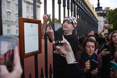 Royal follower John Loughrey, wearing a Union Jack hat, photographs the official announcement of the queen's death. EPA