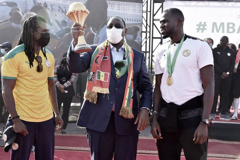 Senegal President Macky Sall, centre, holds the Africa Cup of Nations trophy flanked by Senegal coach Aliou Cisse, left, and captain Kalidou Koubaly in Dakar on Monday, February 7, 2022. AFP