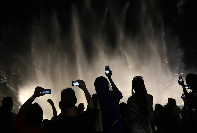 Tourists take photos of the water and light show at the Burj Khalifa. Satish Kumar / The National
