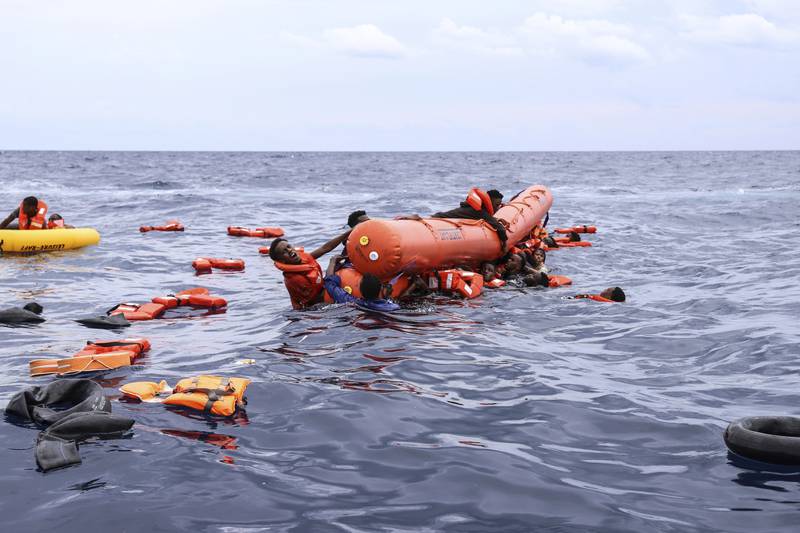 Migrants hold on to the rubber vessel and wait to be rescued.