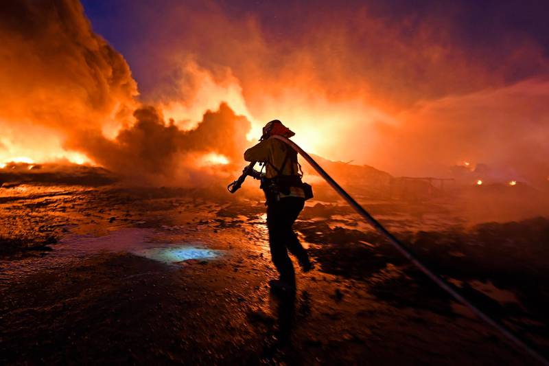 A firefighter drags a hose closer to battle a grass fire in Knightsen, California.