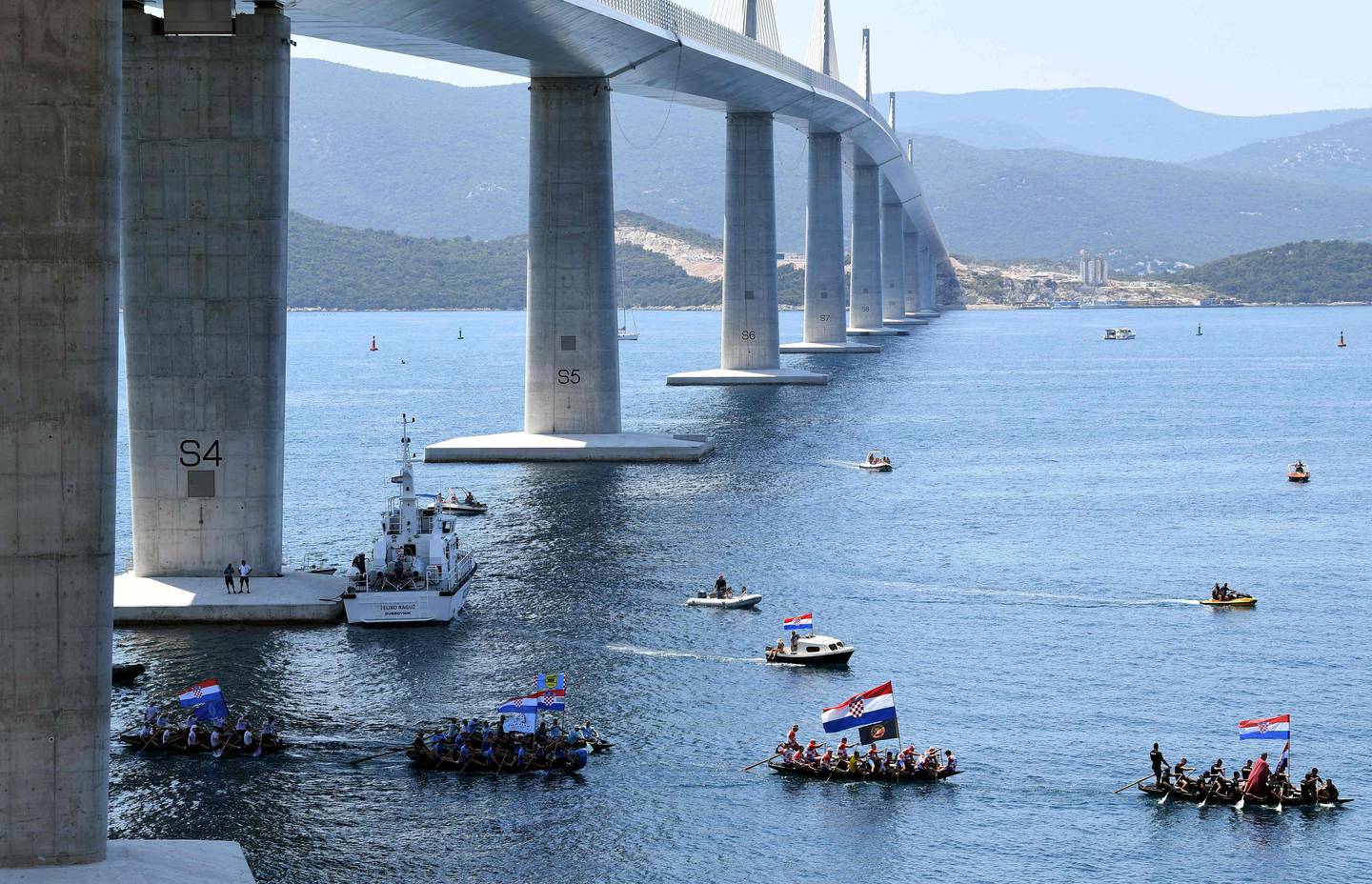 Croatian citizens fly their national flag as they sail in traditional rowing boats beneath the new construction. AFP.