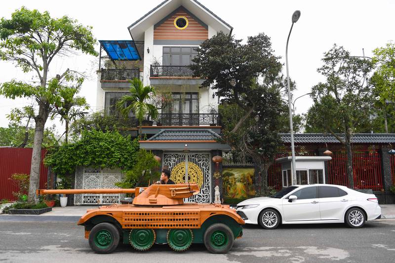 A Vietnamese father who spent hundreds of hours converting an old minibus into a wooden tank for his son - an unusual hobby in a country once ravaged by war - rides past a house in Bac Ninh province.  AFP