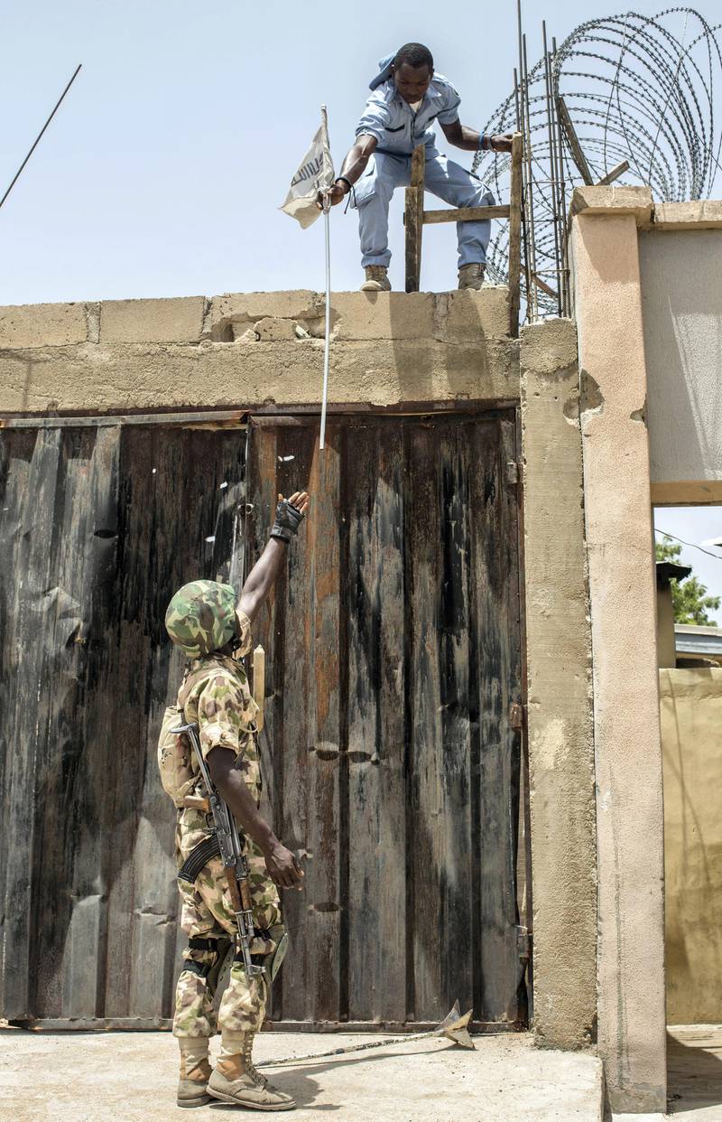 A civilian removes a flag placed by Boko Haram and hands it to a Nigerian army soldier in Bama on March 25, 2015. Nigeria's military has retaken the northeastern town of Bama from Boko Haram, but signs of mass killings carried out by Boko Haram earlier this year remain.  AFP PHOTO / NICHOLE SOBECKI (Photo by Nichole Sobecki / AFP)