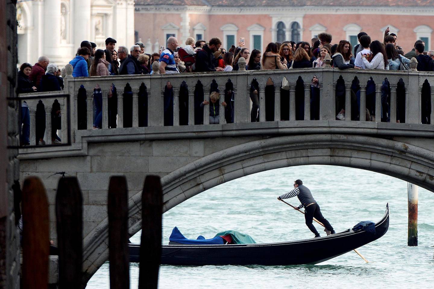 FILE PHOTO: Tourists walk on a bridge as a gondolier rows his gondola near St.Marks Square in Venice, Italy, April 2, 2019. REUTERS/Guglielmo Mangiapane/File Photo