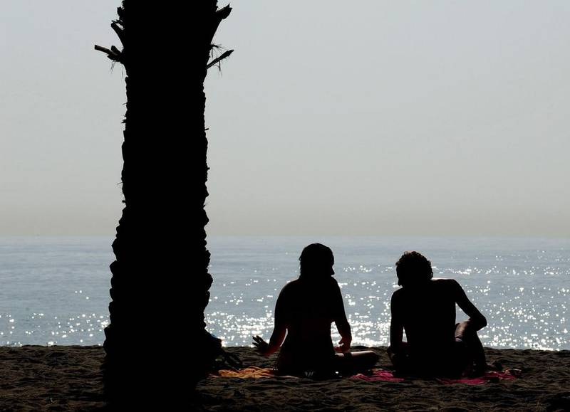 A couple enjoy fine weather next to a palm tree at the usually packed Costa del Sol Carihuela beach in Spain. Jasper Juinen / Getty Images