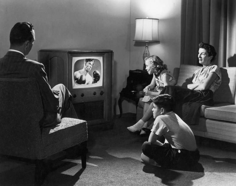 CIRCA 1948: A family of four watches a boxing match on television while sitting together in their living room.  (Photo by Camerique Archive/Getty Images)