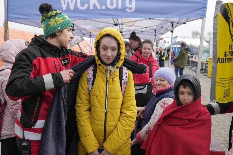 A volunteer covers a refugee with a blanket as she queues at the border crossing in south-eastern Poland. AP Photo