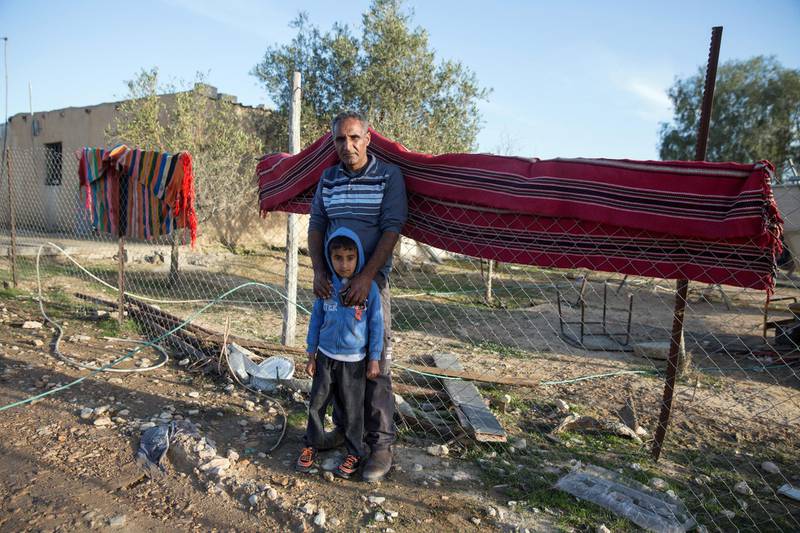 Ali Galboa stands with his son against one of the traditional carpet hanging from the fence that surround his home  in the unrecognized village of al-Poraa near the city of Arad in the Negev Desert on February 4,2018. 
Although he says that the planned giant phosphate is believed to be located several kilometers away from his home, he fear it will bring clouds of toxic fumes and risks to his children who attend school in the area it is believed it will be built.
(Photo by Heidi Levine for The National).
