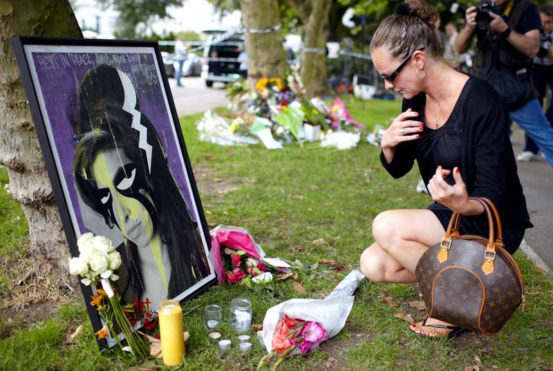 epa02839070 A women pays her respects in front of a painting of singer Amy Winehouse in front of her house in north London, Britain, 24 July 2011. Reports state that British singer Amy Winehouse has been found dead in her London apartment, on 23 July 2011. The 27-year-old was found by the emergency services. Her death was reportedly being treated as 'unexplained.'  EPA/KERIM OKTEN *** Local Caption ***  02839070.jpg