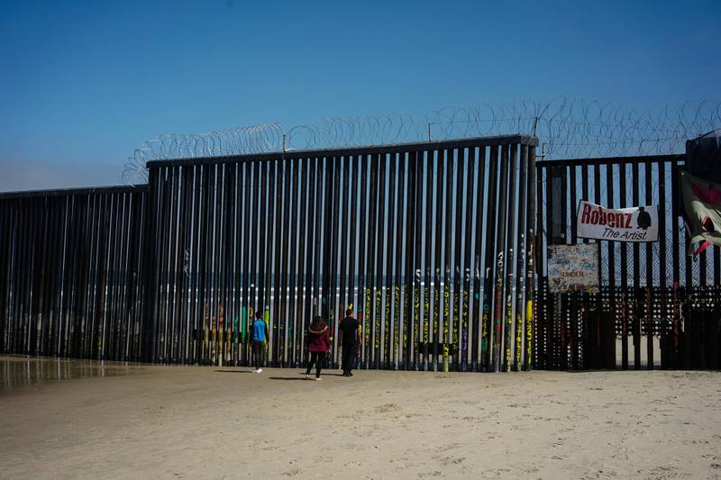 People look through a section of the U.S. and Mexico border wall on the beach in Tijuana, Mexico, on Sunday, June 9, 2019. U.S. President Donald Trump threatened tariffs on Mexico if the country didn't do more to curb the flow of migrants coming from Central America through Mexico to the U.S. -- after also cutting aid to the region. Photographer Cesar Rodriguez/Bloomberg