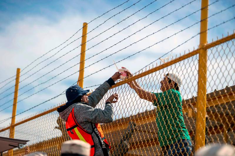 Central American migrants pass food through the fence.  AFP