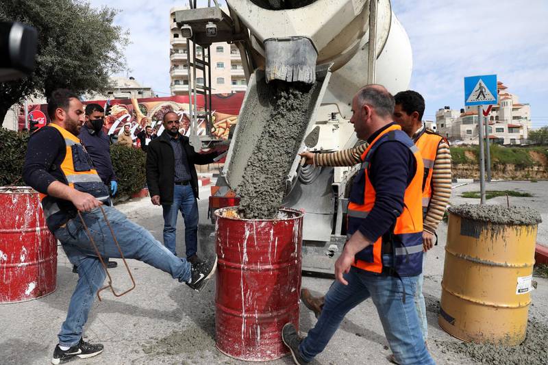 Palestinian workers fill barrels with cement to be used to block roads as part of measures to limit movement in the West Bank city of Hebron.  EPA