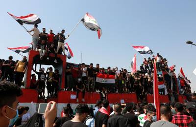 Protesters carry the Iraqi national flag as they stand on concrete blocks which are used by security forces to block the Al-Jumhuriya bridge, close to Tahrir square in central Baghdad. EPA
