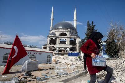 A girl carries a box of water bottles next to a damaged mosque in Antakya. Reuters