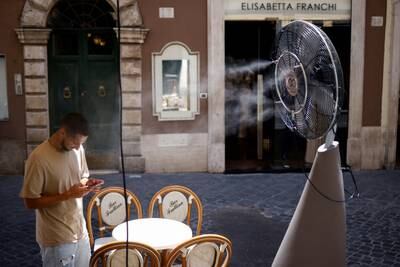 A man cools off in front of a fan as he checks his phone in Rome as Italy swelters. Reuters