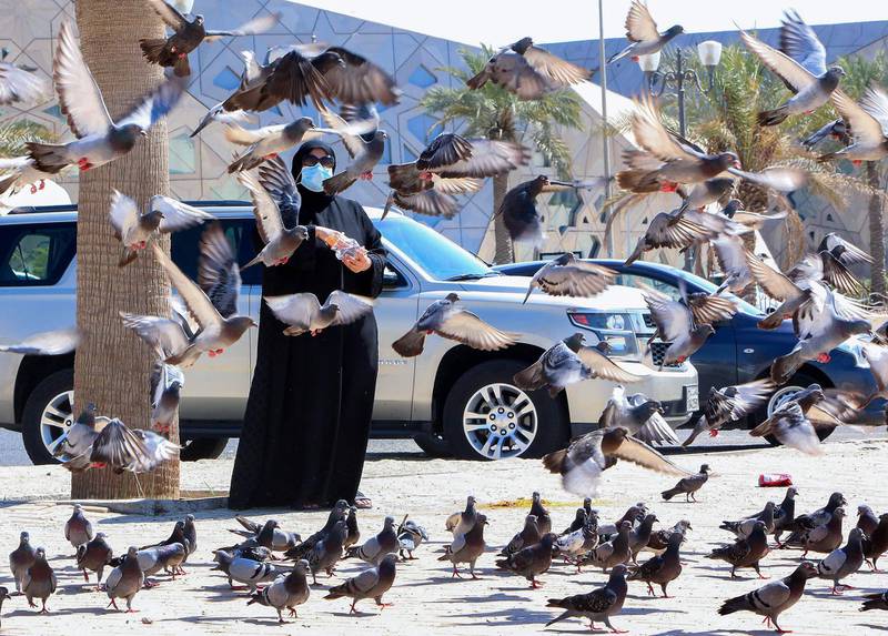 A Kuwaiti woman wearing a protective mask amid the COVID-19 pandemic feeds pigeons at a square in Kuwait City. AFP