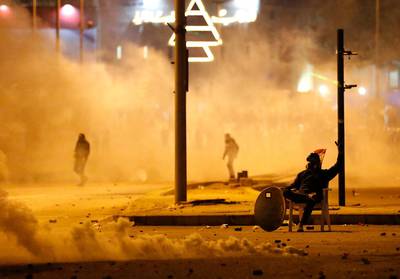 An anti-government protester covered by the smoke of the tear gas, sits in the middle of a street. AP Photo