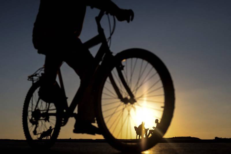 A Palestinian man rides his bicycle as others sit together by the beach during sunset in Gaza city. AFP