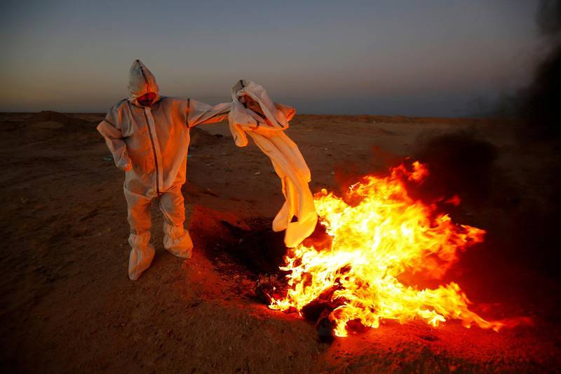 A member of the Popular Mobilization Forces (PMF), who volunteered to work in a cemetery, wears a protective suit, as he burns clothes they used for burial, near the new Wadi Al-Salam cemetery, which is dedicated to those who died of the coronavirus disease (COVID-19), on the outskirts of the holy city of Najaf, Iraq May 25, 2020. Picture taken May 25, 2020. REUTERS/Alaa al-Marjani     TPX IMAGES OF THE DAY