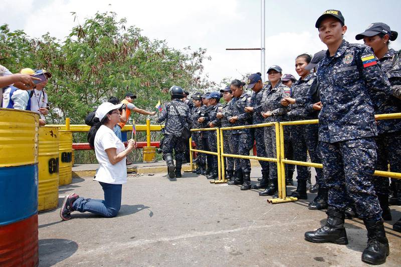 A supporter of Venezuela's opposition leader Juan Guaido kneels in front of police standing guard at the Francisco de Paula Santander International Bridge. AFP