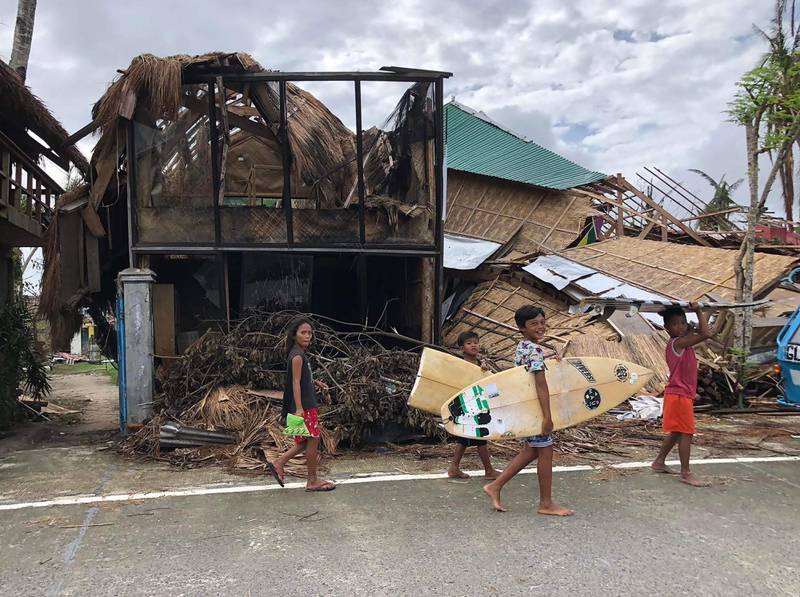 Young surfers pass houses destroyed by super Typhoon Rai on their way to the beach in General Luna town, Siargao island. AP