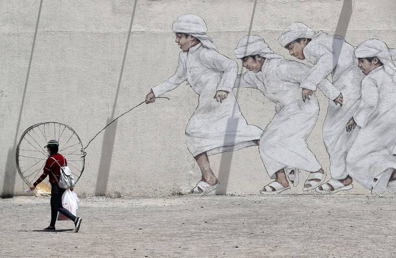 DUBAI, UNITED ARAB EMIRATES , June 11 – 2020 :- A woman wearing face mask and passing by the art work of Emirati boys playing in Al Satwa area in Dubai. (Pawan Singh / The National) For Standalone/Instagram/Big Picture