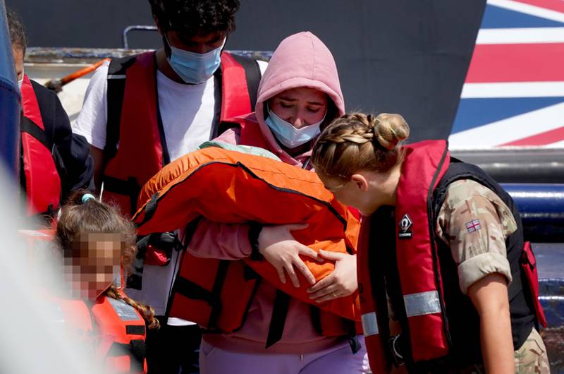 A woman carries a newborn baby in a life cradle as she is brought in to Dover, Kent, on a Border Force vessel in July. PA