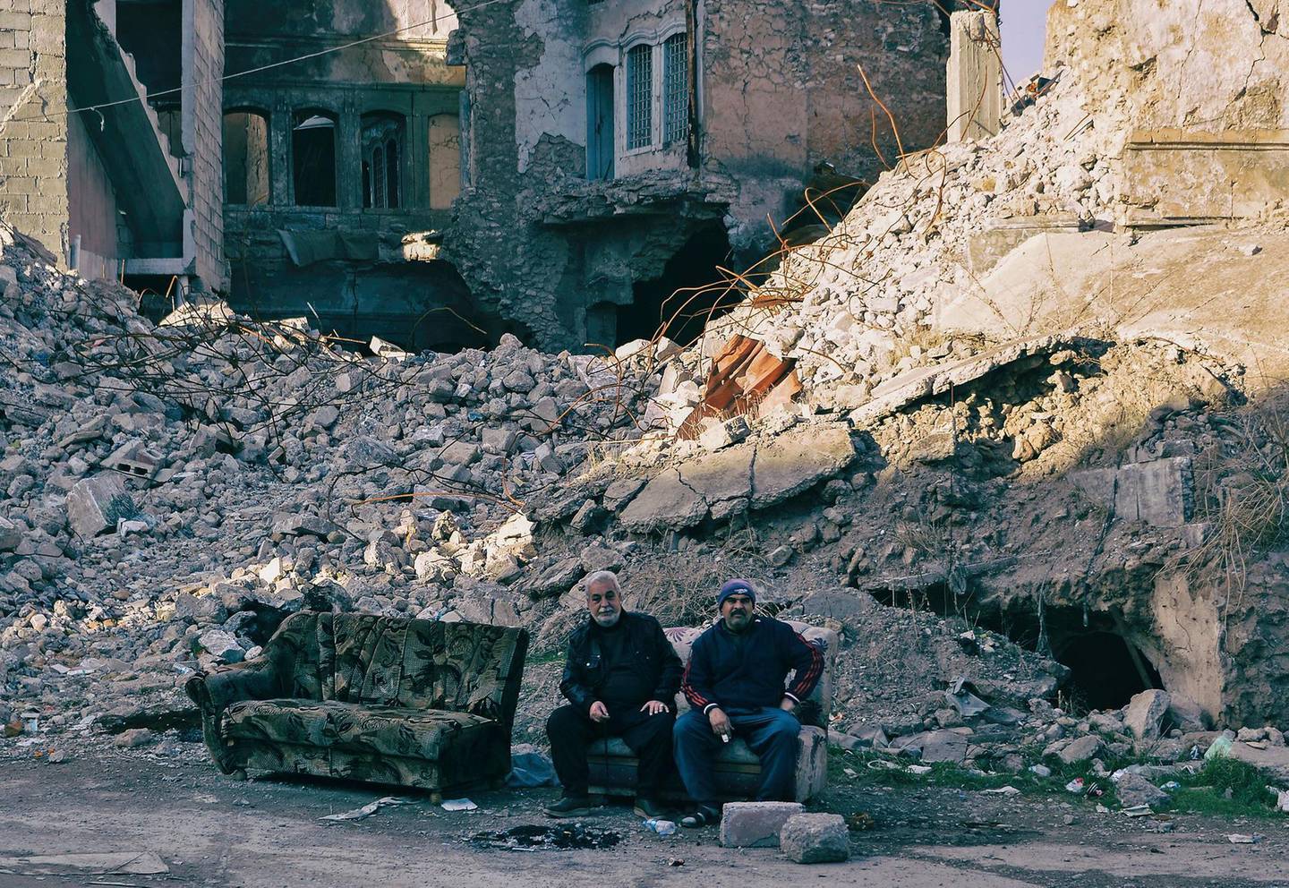 Iraqi men sit amidst debris of destroyed buildings in Iraq's northern city of Mosul on January 18, 2021. Once the historic heart of Iraq's Mosul, the Old City has lain in ruins for years. With rebuilding unlikely and the economy in a tailspin, homeowners are itching to sell. The single-family homes along the banks of the river Tigris, which divides Mosul in two, have remained largely untouched since Iraqi troops ousted the Islamic State group from the northern city in the summer of 2017. / AFP / Zaid AL-OBEIDI
