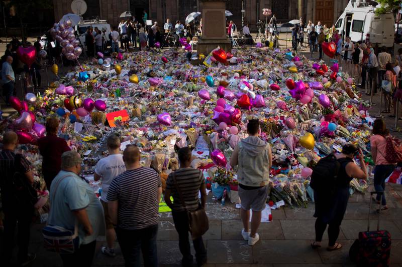 FILE - In this Friday, May 26, 2017 file photo, people stand next to tributes placed in St Ann's Square in central Manchester, England, after Monday's bombing. A major British parliamentary report found Thursday Nov. 22, 2018, that shortcomings by security services led to missed opportunities to possibly prevent last year's lethal extremist attack at Manchester Arena. (AP Photo/Emilio Morenatti, File)