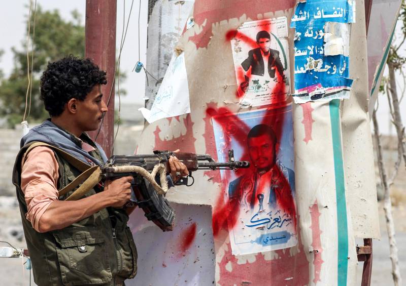 A Yemeni fighter from the Amalqa ("Giants") Brigades loyal to the Saudi-backed government stands pointing a Kalashnikov assault rifle towards a crossed-out plastered poster of the Houthi rebel leader Abdulmalik al-Houthi, on the southern outskirts of the Red Sea port city of Hodeidah near the airport on June 21, 2018. Saleh Al-Obeidi / AFP