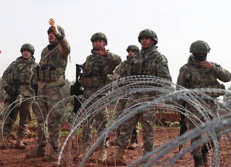 Turkish soldiers stand behind barbed wire at a Turkish military observation post in the town of Binnish in Syria’s northwestern province of Idlib, in the Syria-Turkey border on February 14, 2020, as people come to demonstrate before them.  / AFP / Omar HAJ KADOUR
