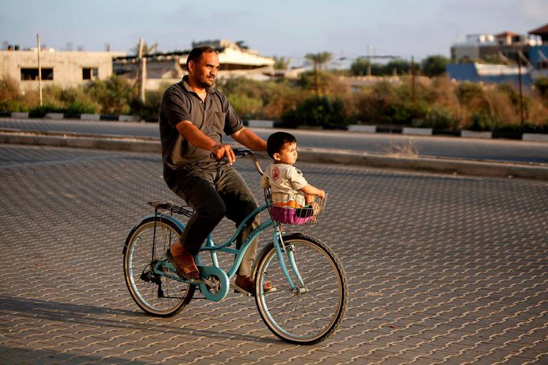 A Palestinian man rides a bicycle with his child in Gaza City as coronavirus lockdown eases.  AFP