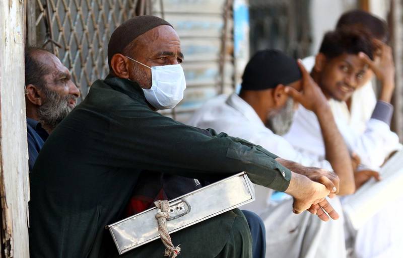 People sit outside a closed market of a restricted area that is sealed in smart lockdown in Karachi, Pakistan. EPA