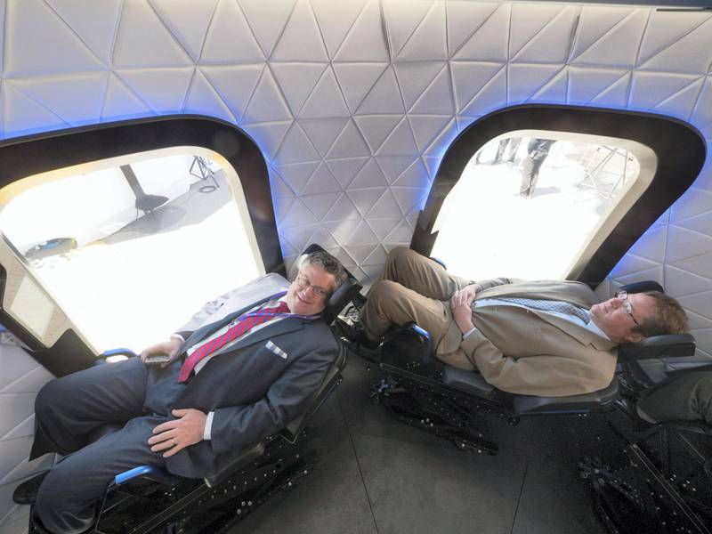Attendees sit inside the high fidelity crew capsule mock up of the Blue Origin LLC New Shepard system during the Space Symposium in Colorado Springs, Colorado, U.S., on Wednesday, April 5, 2017. Jeff Bezos, chief executive officer of Amazon.com Inc. and founder of Blue Origin, has been reinvesting money he made at Amazon since he started his space exploration company more than a decade ago, and has plans to launch paying tourists into space within two years. Photographer: Matthew Staver/Bloomberg