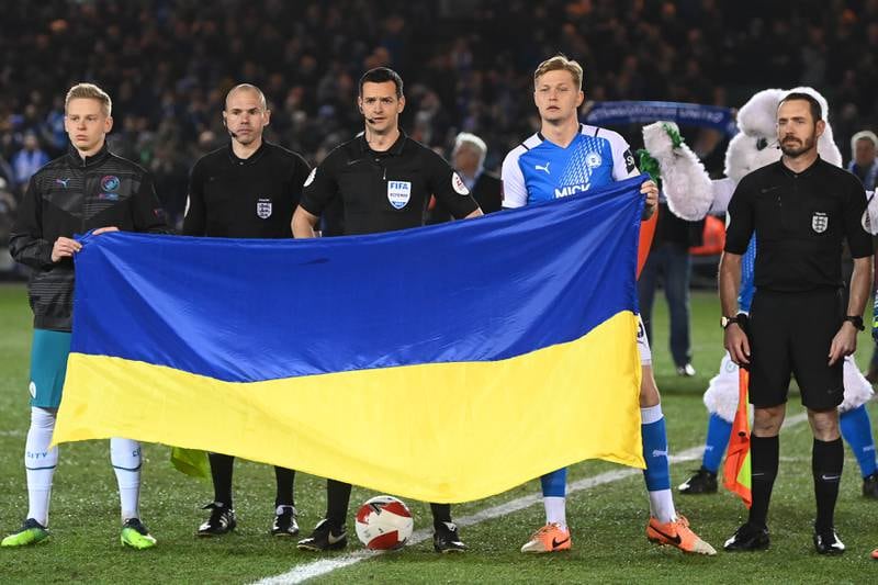 Oleksandr Zinchenko of Manchester City, referee Andy Madley and Frankie Kent of Peterborough United hold a Ukrainian flag to indicate peace and sympathy with Ukraine. Getty