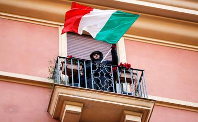 epa08319512 A boy with an Italian tricolor flag stands on a balcony during a flash mob launched across Italy to bring people together and try to cope with the emergency of the coronavirus, in Rome, Italy, 24 March 2020.  EPA/Riccardo Antimiani