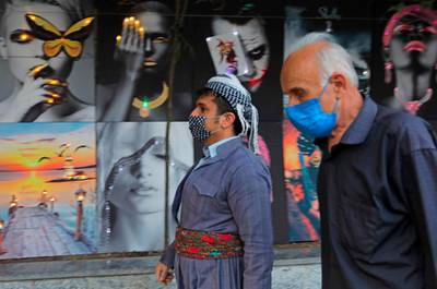 Mask-clad men walk past posters in the vicinity of Arbil Citadel in the capital of the northern Iraqi Kurdish autonomous region.  AFP