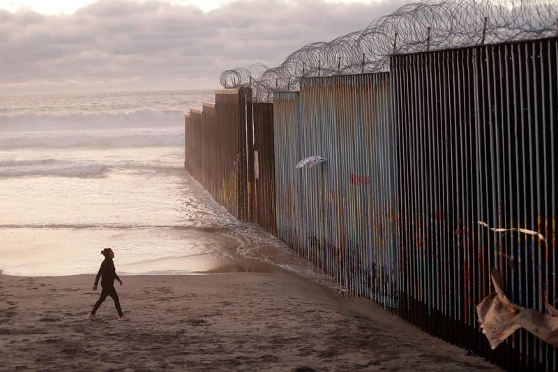 FILE - In this Jan. 9, 2019 file photo, a woman walks on the beach next to the border wall topped with razor wire in Tijuana, Mexico. What started as an online fundraiser to provide President Donald Trump with donations for his southern border wall has morphed into a new foundation whose members vow to build a wall themselves.  The "We The People Will Build the Wall" campaign has surpassed $20 million since it was created in December by Air Force veteran and triple amputee Brian Kolfage. The campaign has received almost 350,000 donations even as wall opponents derided the effort and after the longest government shutdown in U.S. history ended with Congress refusing Trump's demand for billions in wall funding.  (AP Photo/Gregory Bull, File)