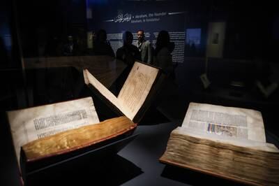 People inspect a Quran, a Torah and a Bible, part of the Letters of Light exhibition at Louvre Abu Dhabi on Monday. EPA